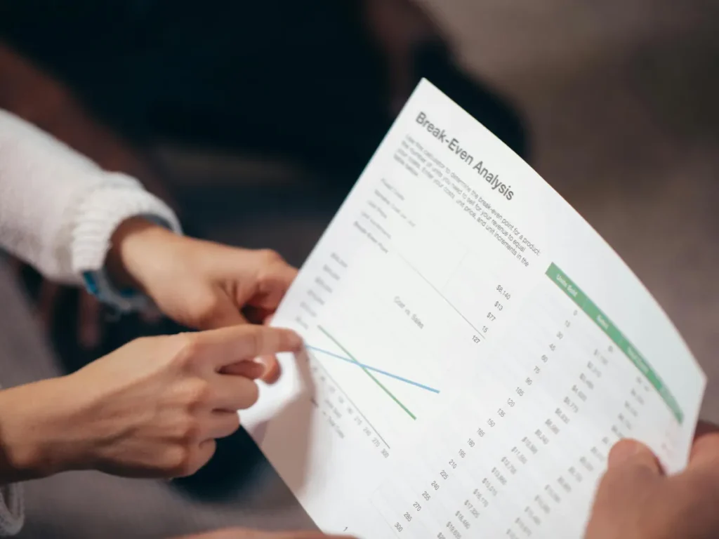 Dua tangan sedang mendiskusikan dokumen analisis break even point dalam rapat bisnis