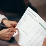 Dua tangan sedang mendiskusikan dokumen analisis break even point dalam rapat bisnis